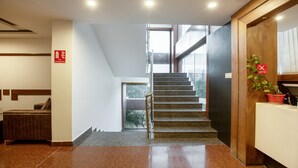 Un interior moderno con una escalera que conduce a un piso superior, un mostrador de recepción y un cartel de extintor.