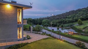 A modern building with a balcony and a view of a river and forested hills. - Kalpavriksha Villa By Indostay (Kotagiri)