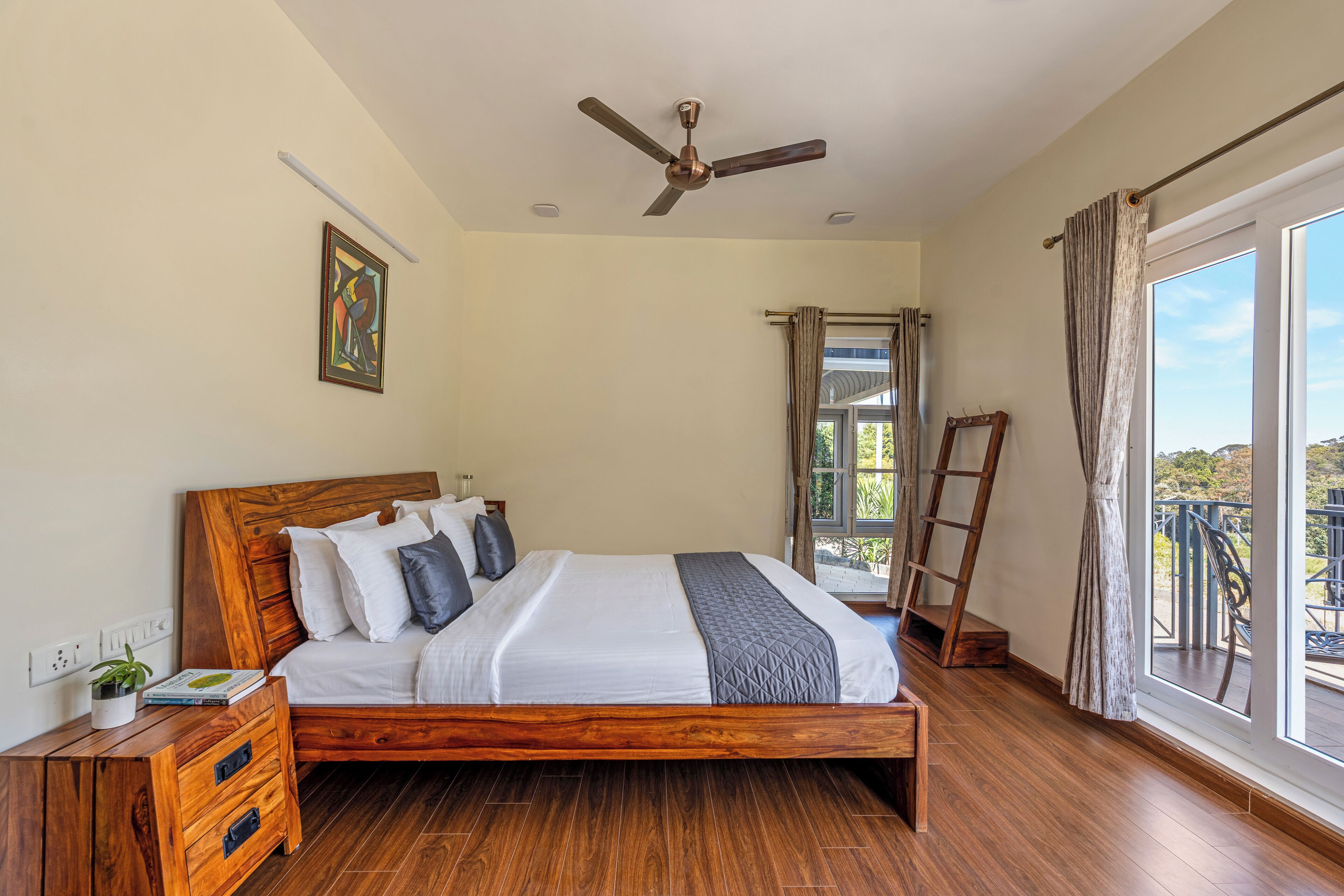 Un dormitorio con cama de madera, ventilador de techo, ventana con cortinas y balcón con vistas.