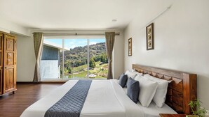 A large bed with a wooden headboard, a view of a lush landscape through a sliding door, and a wooden wardrobe. - Kalpavriksha Villa By Indostay (Kotagiri)
