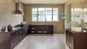 A modern kitchen with dark cabinets, a stainless steel range hood, and a window providing natural light. - Kalpavriksha Villa By Indostay (Kotagiri)