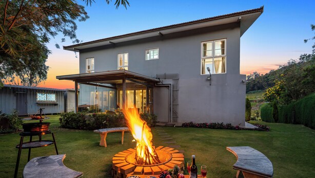 A modern house with a fire pit in the backyard, surrounded by outdoor furniture and a dining table with food and drinks. - Kalpavriksha Villa By Indostay (Kotagiri)