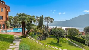 A pool area with stone pathways, lush greenery, and a view of the sea and mountains.