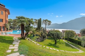 A pool area with stone pathways, lush greenery, and a view of the sea and mountains.