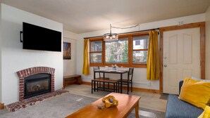 Un salon avec une cheminée, une table à manger avec des chaises, un canapé et un téléviseur fixé au mur.