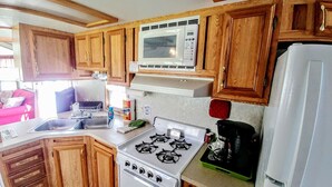 A compact kitchen with wooden cabinets, a white stove, a microwave, and a refrigerator.
