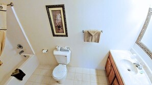 A bathroom with a bathtub, toilet, sink, and a framed picture on the wall.