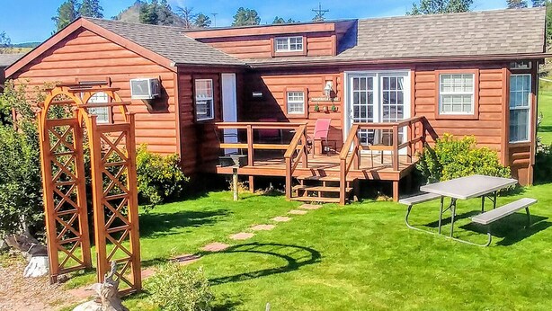 A log cabin with a deck, picnic table, and a wooden archway.