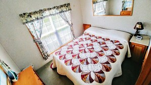A bedroom with a large bed, a window with curtains, a bedside table with a lamp, and a mirror on the wall.