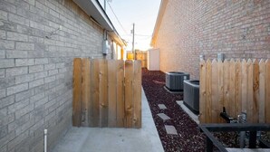 A narrow outdoor corridor with brick walls, wooden gates, and a gravel path. - 1BR Sleeps 4 | AI Data Ctr, Hospitals, Corp Stays (Amarillo)