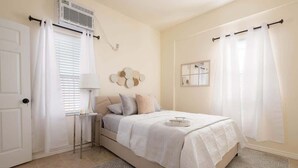 A bedroom with a bed, bedside table, lamp, air conditioning unit, and a mirror on the wall. - 1BR Sleeps 4 | AI Data Ctr, Hospitals, Corp Stays (Amarillo)
