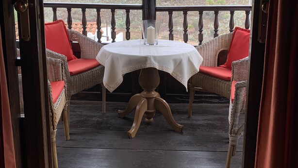 Un espace extérieur abrité, avec une table et des chaises en osier, offrant une vue sur un paysage vallonné.