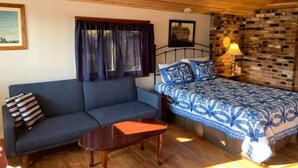A cozy room with a blue sofa, a bed with a patterned blue and white bedspread, a wooden coffee table, and a brick wall. - Best View of the Lake in Harrison (Harrison)