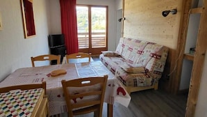 A cozy room with a wooden sofa, a dining table with chairs, and a television.