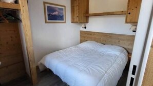 A bedroom with a wooden headboard, a single bed, a small shelf with items, and a framed picture on the wall.