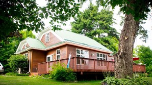 A two-story house with a green roof, a covered porch, and a large tree in the front yard. - Entire Home located in historical district (Bayfield)