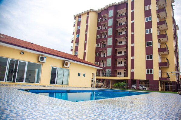 A residential building with a swimming pool, balconies, and a tiled roof.