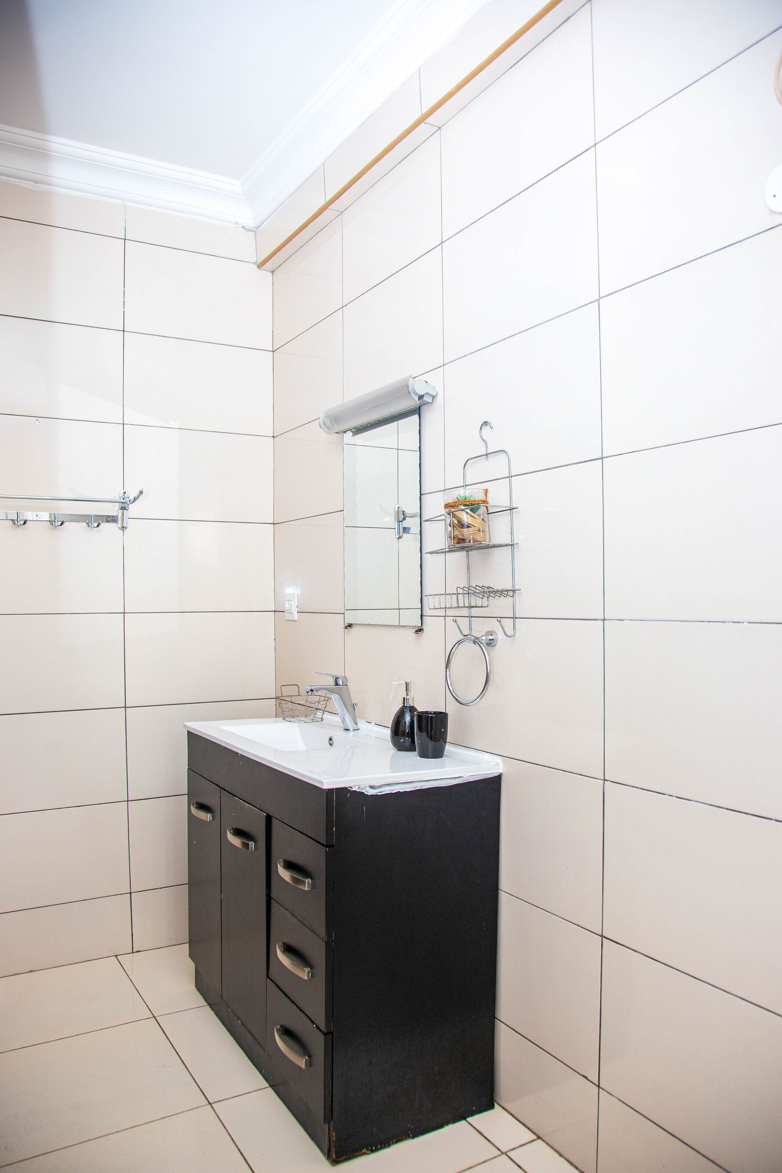 A bathroom with white tiled walls, a black vanity with a sink, and a mirror above it.
