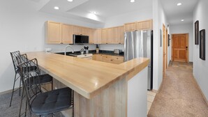A modern kitchen with wooden cabinets, stainless steel appliances, a central island with bar stools, and recessed lighting. - The Corral at Breckenridge #206S By Summit County Mountain Retreats (Breckenridge)