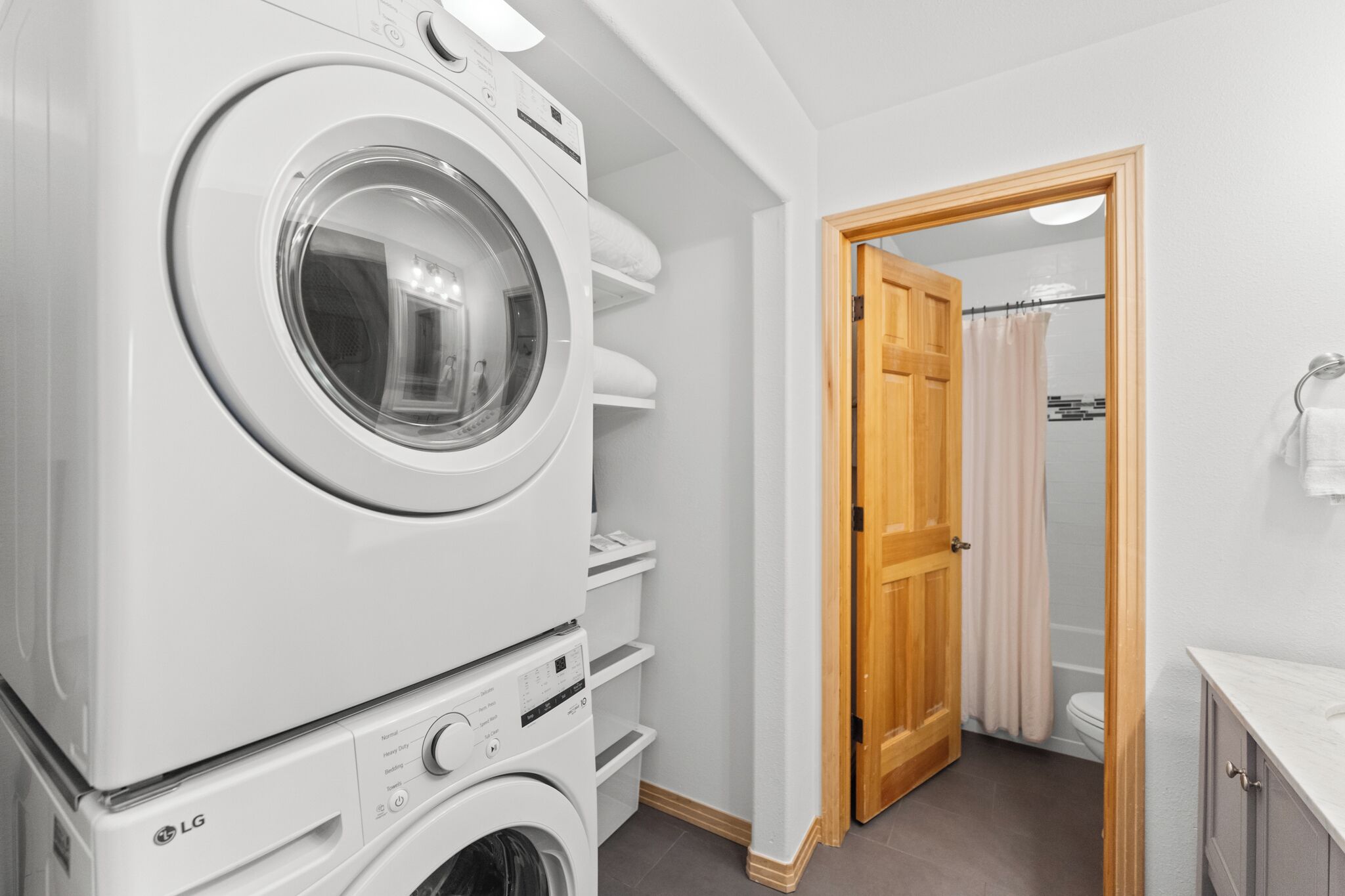 A laundry room with stacked washing machines and dryers, a wooden door leading to a bathroom, and a small countertop with a sink.