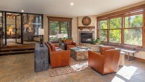 A spacious living room with leather sofas, a fireplace, large windows, and a stone fireplace surround. - The Corral at Breckenridge #206S By Summit County Mountain Retreats (Breckenridge)