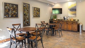 A dining area with round wooden tables and metal chairs, a kitchen with wooden cabinets, and artwork on the walls. - The Corral at Breckenridge #206S By Summit County Mountain Retreats (Breckenridge)