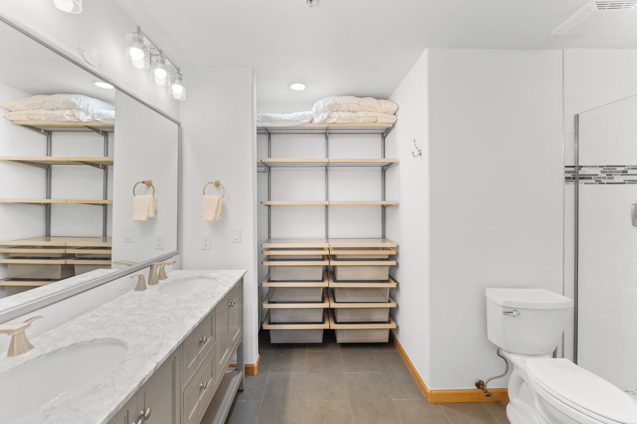 Un baño moderno con un espejo grande, lavamanos dobles y estantes de almacenamiento integrados.