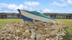 A boat resting on a pile of rocks in front of a row of buildings with a clear sky. - MotorBoat Inn Suite 10 (Graford)