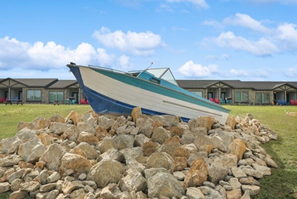 A boat resting on a pile of rocks in front of a row of buildings with large windows.