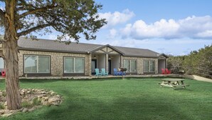 A stone house with a large front porch, a covered patio, and a well-maintained lawn. - MotorBoat Inn Suite 14 (Graford)