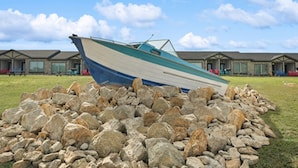 A boat resting on a pile of rocks in front of a row of buildings with a clear sky. - MotorBoat Inn Suite 15 (Graford)