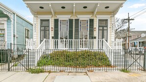 A two-story house with a white facade, green shutters, and a small front porch. - Irish Channel Stunner! (New Orleans)