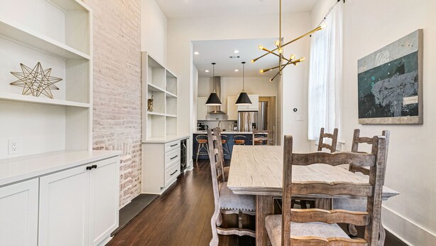 A modern kitchen with white cabinetry, a brick accent wall, and a dining area with wooden chairs and a table. - Irish Channel Stunner! (New Orleans)