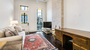 A living room with a sofa, TV, desk, and a red patterned rug. - Irish Channel Stunner! (New Orleans)