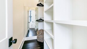 A narrow hallway with white shelving units, a black door, and a wicker basket on the floor. - Irish Channel Stunner! (New Orleans)