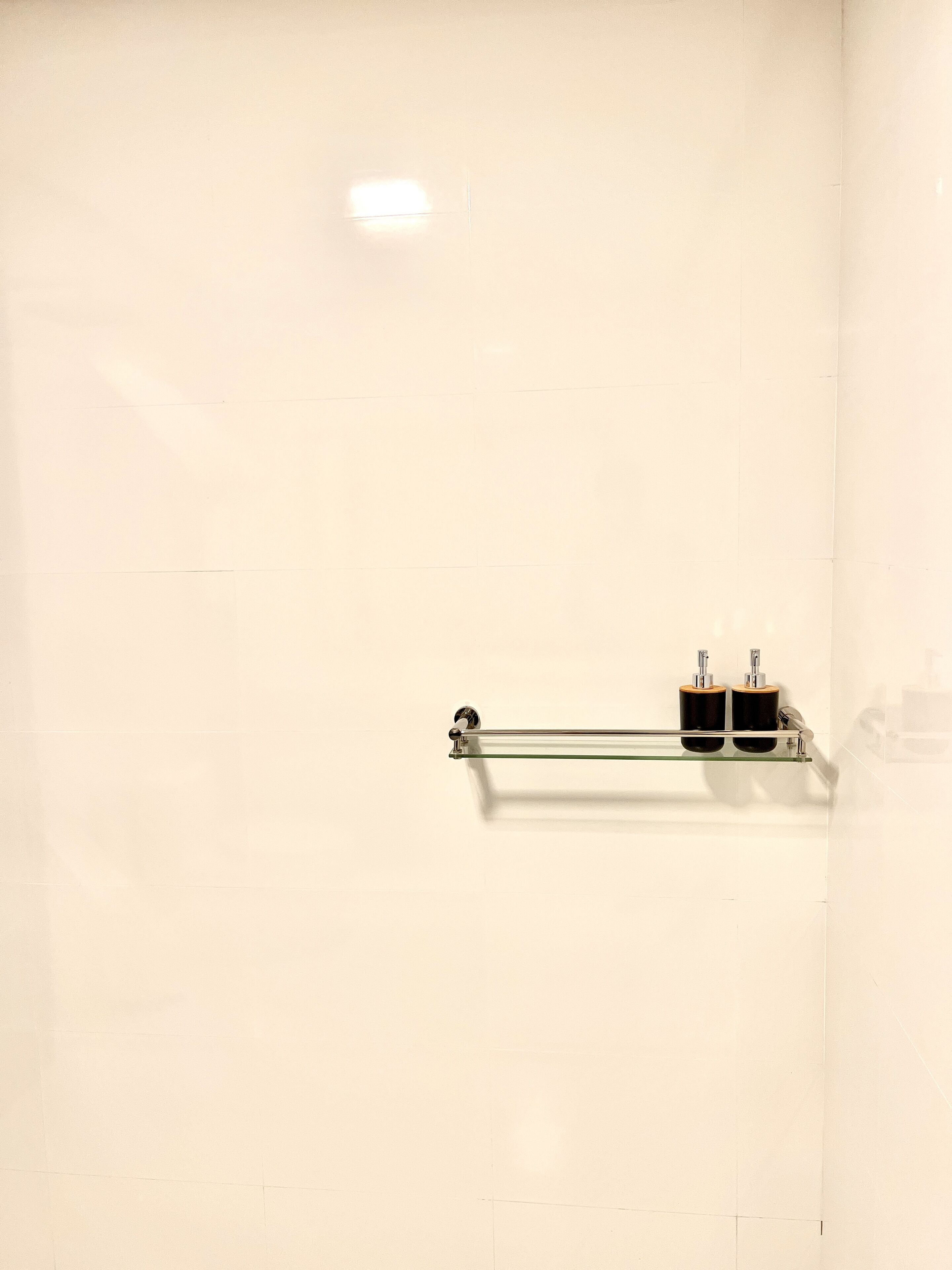 Baño con repisa de vidrio que sostiene dos botellas negras y una barra de vidrio.
