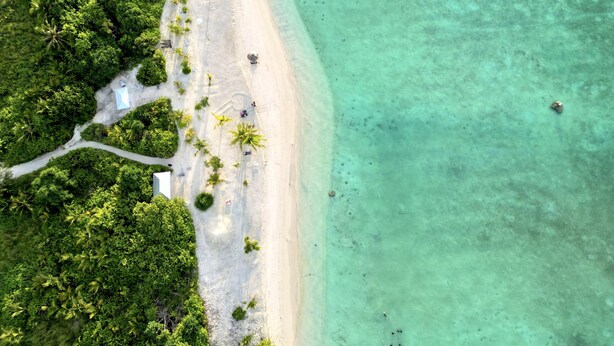 An aerial view of a beach with clear turquoise water, surrounded by dense green foliage. - Vilu Residence (Maamigili)