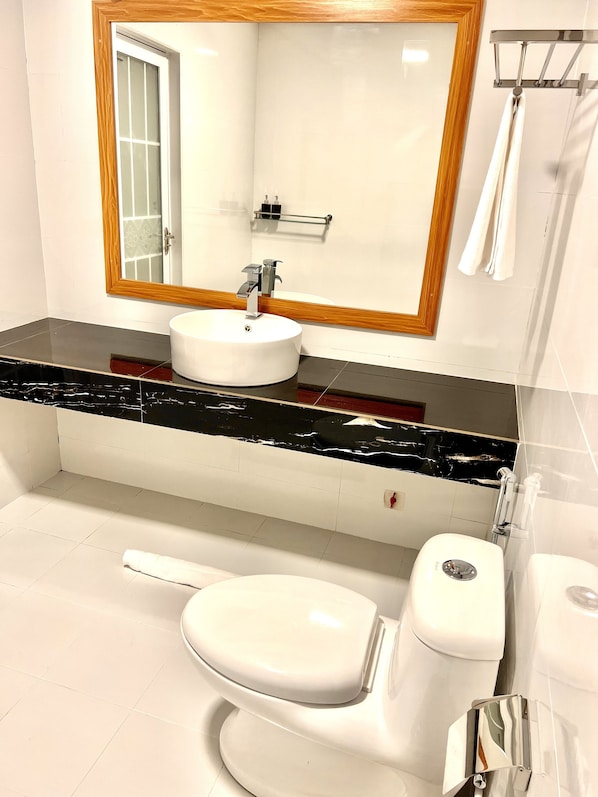 A bathroom with a white sink, a mirror with a wooden frame, a toilet, and a shower area. - Vilu Residence (Maamigili)