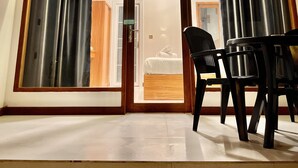 A room with a wooden ceiling, a sliding glass door leading to a bedroom, and a table with chairs. - Vilu Residence (Maamigili)