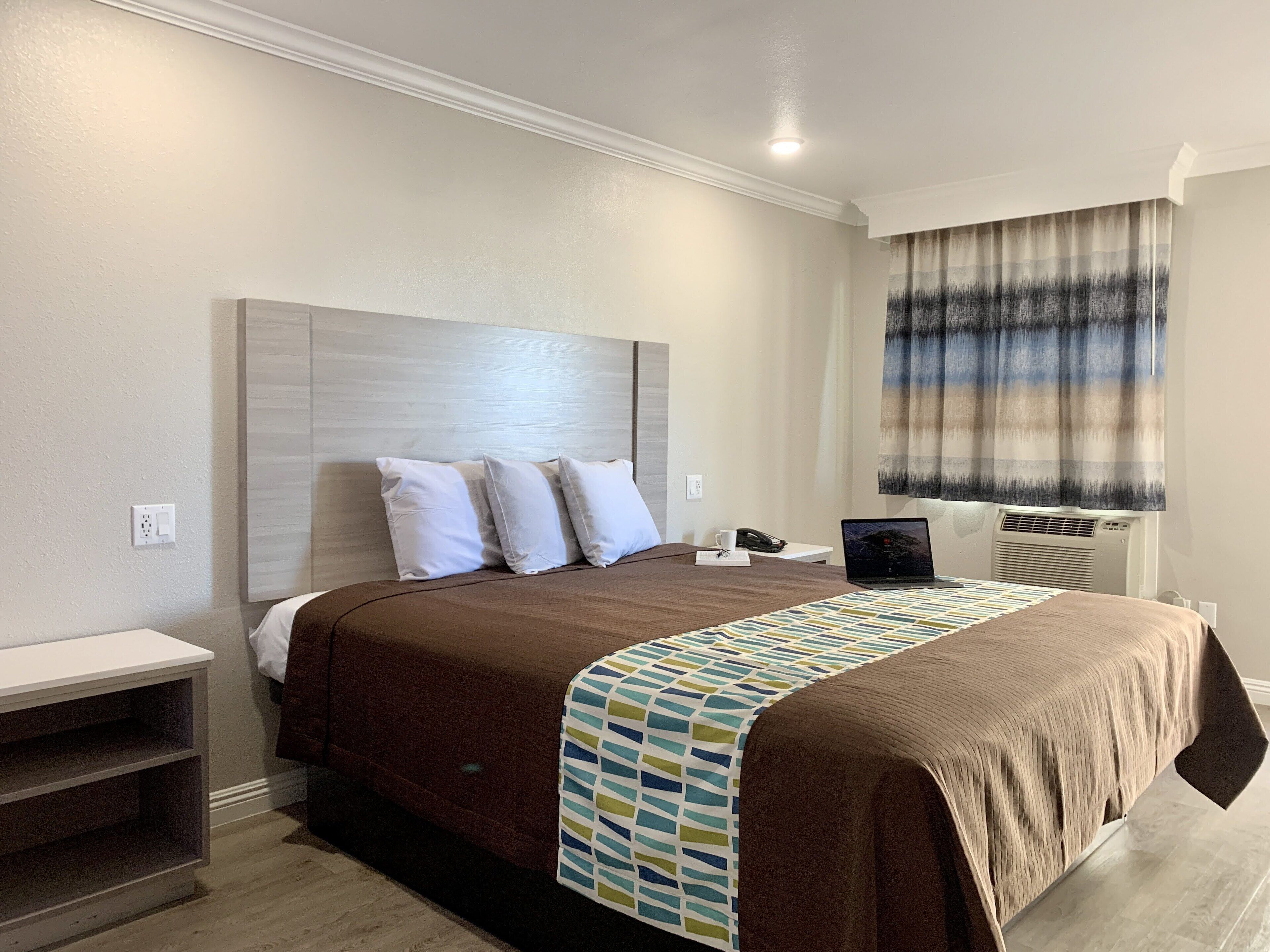 Une chambre d’hôtel bien aménagée, avec un grand lit, une table de chevet, un bureau avec un ordinateur portable et une fenêtre avec des rideaux.