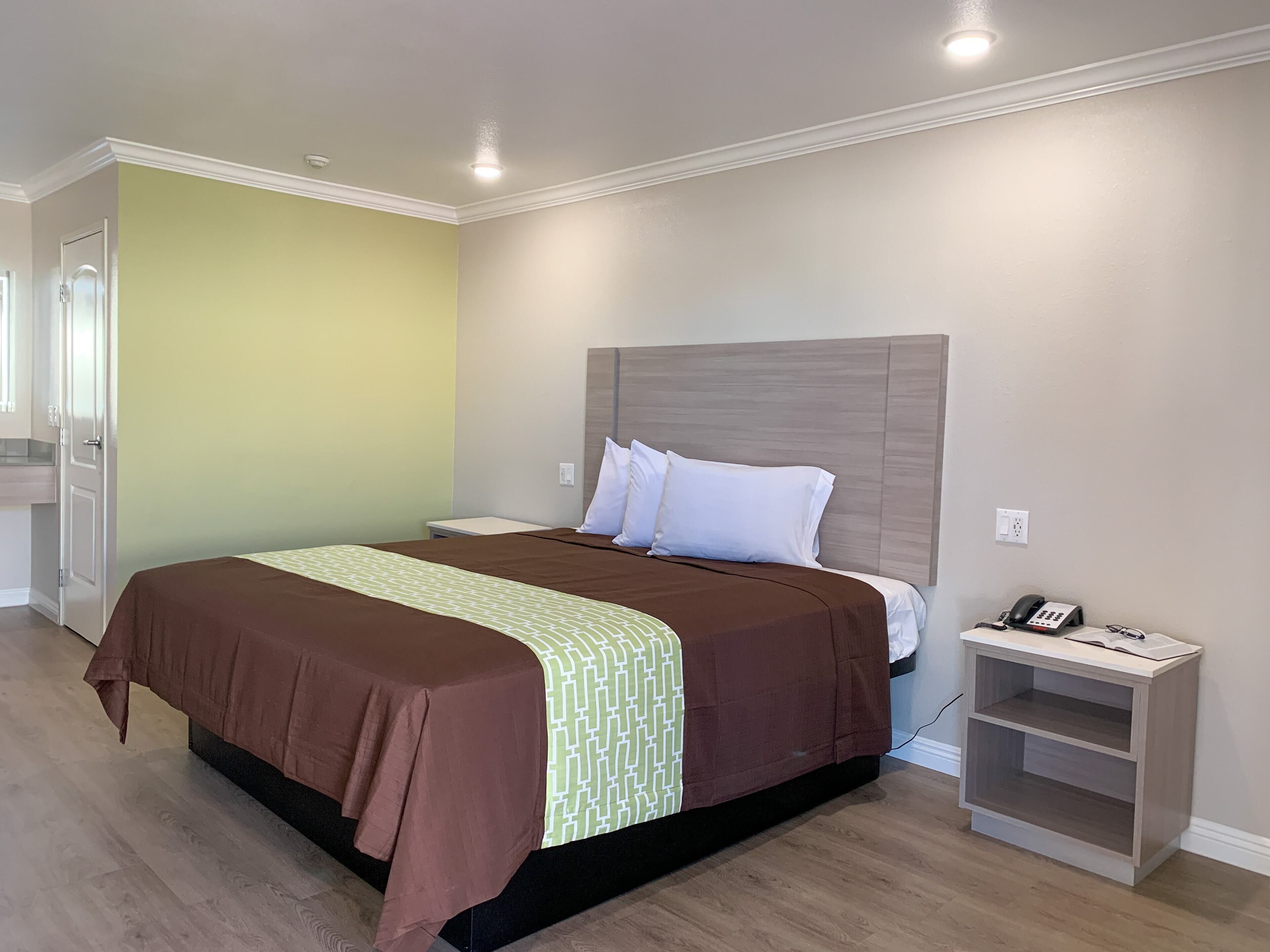Quarto de hotel com cama, mesa de cabeceira e pequeno armário.