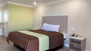 Quarto de hotel com cama, mesa de cabeceira e pequeno armário.