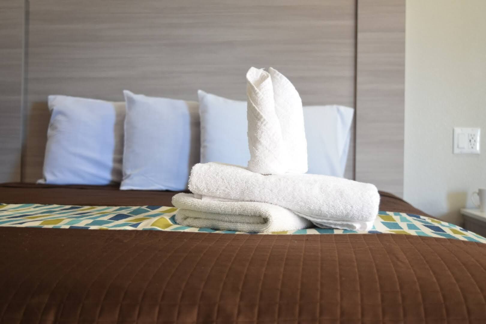 Ein ordentlich bezogenes Bett mit braunem Kopfteil, weißen Kissen und einem gefalteten weißen Handtuch.