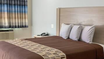 Ett hotellrum med en stor säng, ett nattduksbord med en telefon och ett fönster med gardiner.
