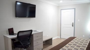 Un dormitorio con una cama, un escritorio con silla, un televisor y una puerta.