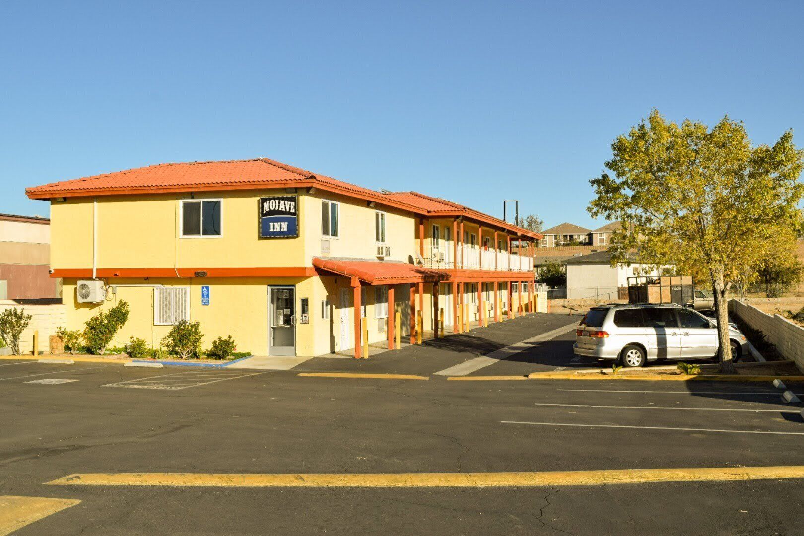 A motel with a red roof, a sign reading "MOJAVE INN," and a parking lot with a few cars.