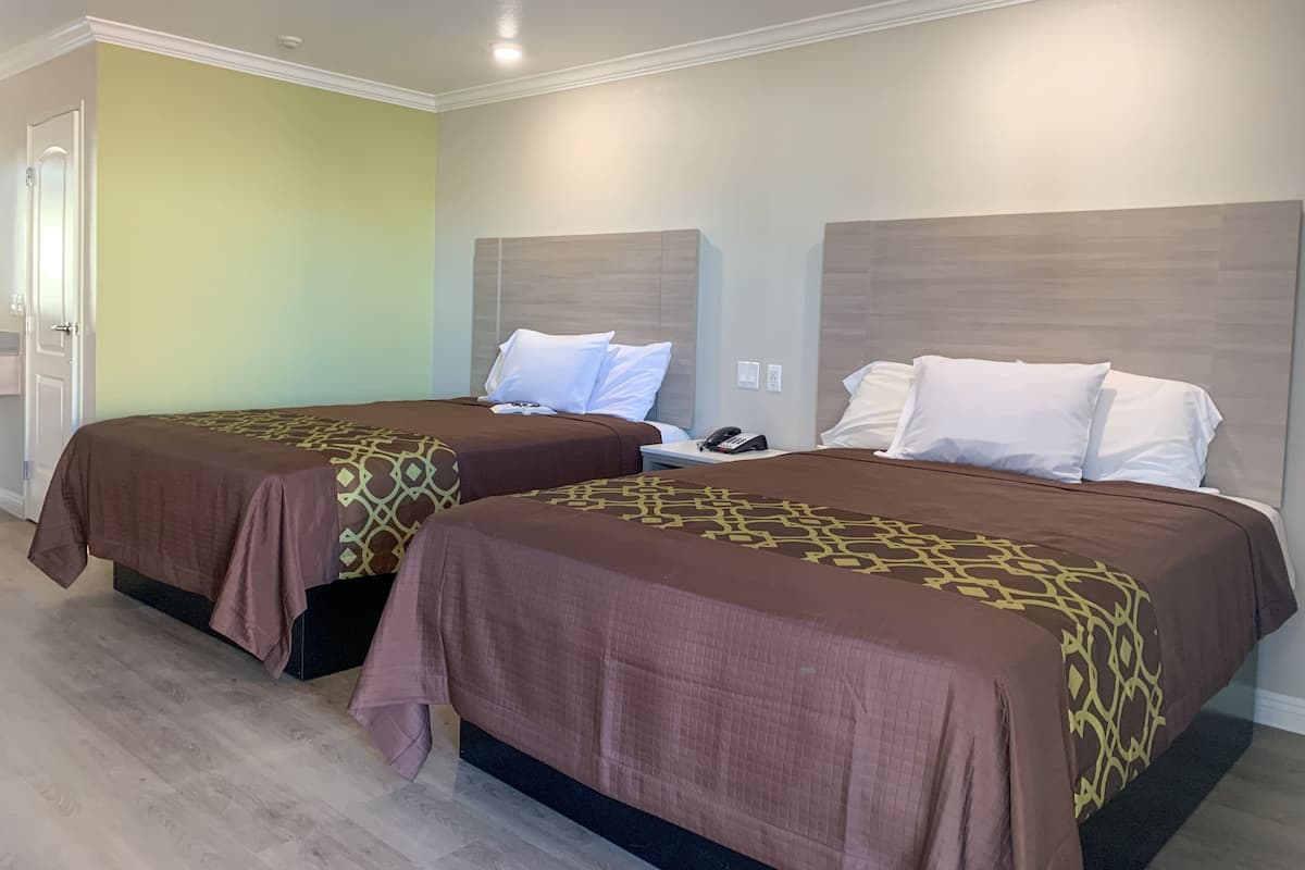 A hotel room with two beds, each with a patterned bedspread, a bedside table with a phone, and a door to the left.
