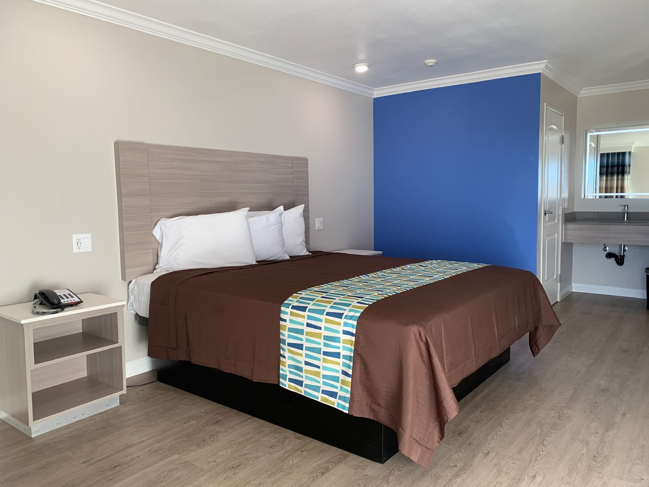 Una habitación de hotel con una cama grande, una mesita de noche con un teléfono y un baño con espejo y lavamanos.