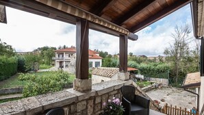 A covered outdoor seating area with stone walls, wicker furniture, and a view of a residential neighborhood. - #914 Home in Irpinia (Nusco)