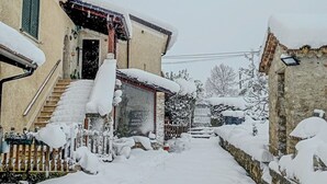 A snow-covered residential area with a house featuring a stone facade and a wooden staircase leading to the entrance. - #914 Home in Irpinia (Nusco)